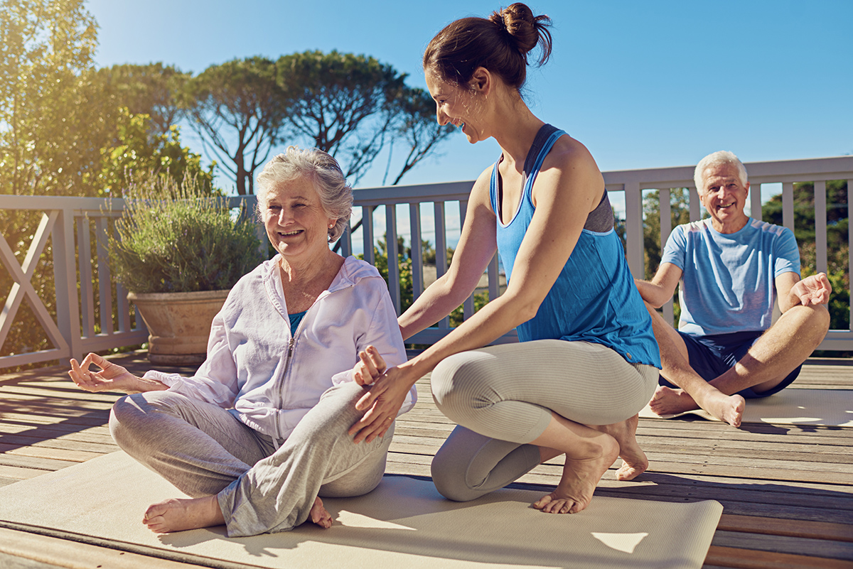 Shot of a senior couple doing yoga together with an instructor on their patio outside.